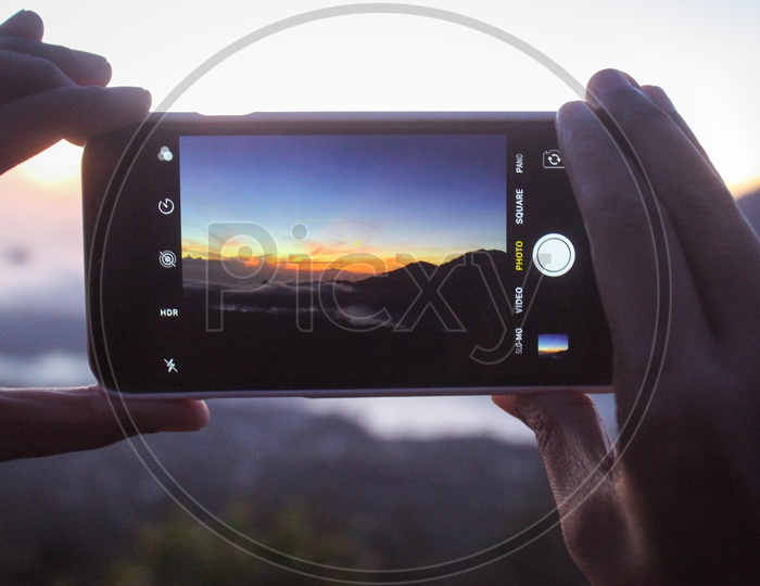 Hands Capturing The Sunset Sky in Smartphone