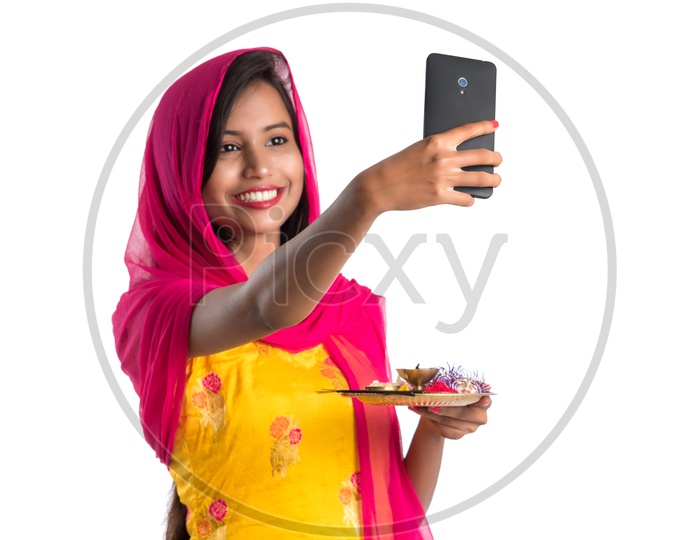Beautiful Indian Girl Holding Pooja Thali Or Pooja Plate  In Hand and Taking Selfie With a Smart Phone