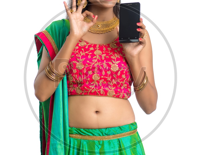 Portrait Of a Young  Traditional Indian  Woman  Showing Smart Phone Screen and  With an Expression an d a Gesture Over a White Background