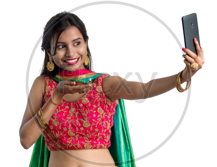 Portrait Of a Young Indian Traditional Woman Holding Dia in Hand and  Taking Selfie in Smart Phone  Over  Isolated White Background