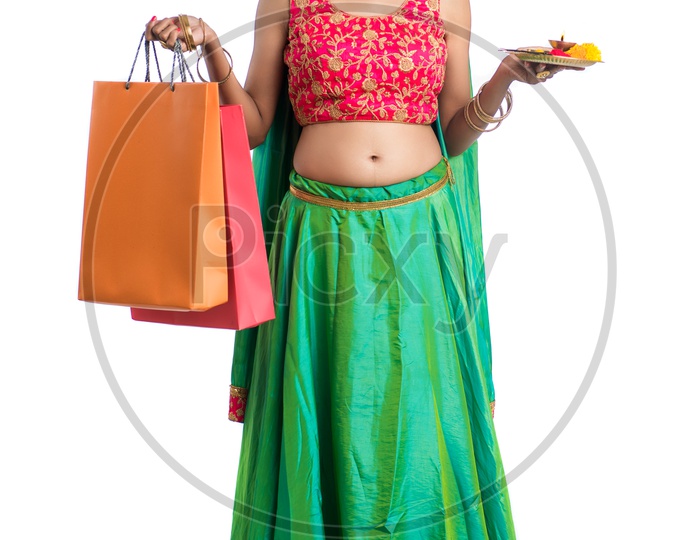 Portrait Of a Young India Traditional Woman  Holding Pooja Plate Or Dia  and Shopping Bags  in Hand  Over a White  Background