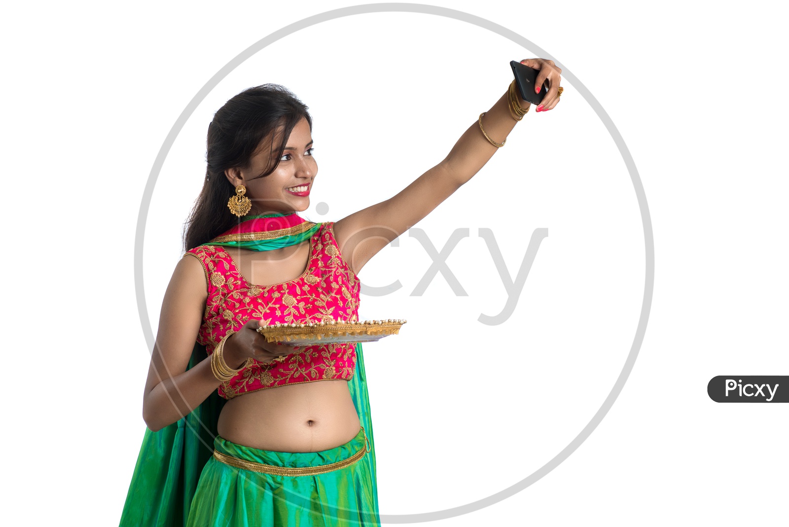 A Young Indian Traditional Girl Taking Selfie In Smart Phone With Dia  or Festival Plate In Hand  Over an Isolated White Background