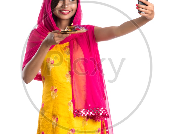 Beautiful Indian Girl Holding Pooja Thali Or Pooja Plate  In Hand and Taking Selfie with Smart Phone