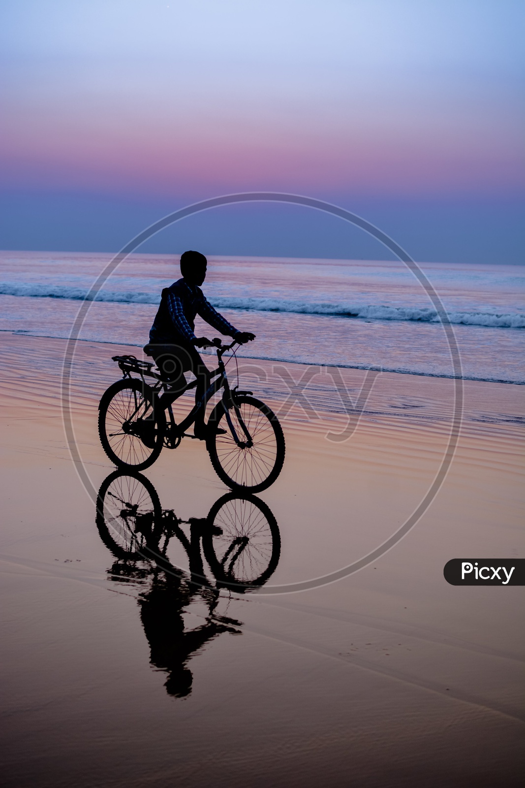Silhouette Of a Boy Cycling in Beach And His Reflection On Water Surface