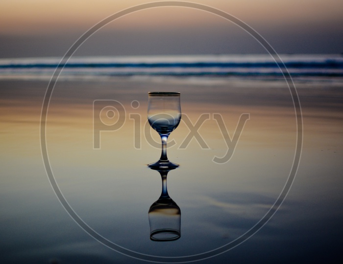 A Wine Glass and Its Reflection On the Beach Water Surface Over a Blue Hour Sky