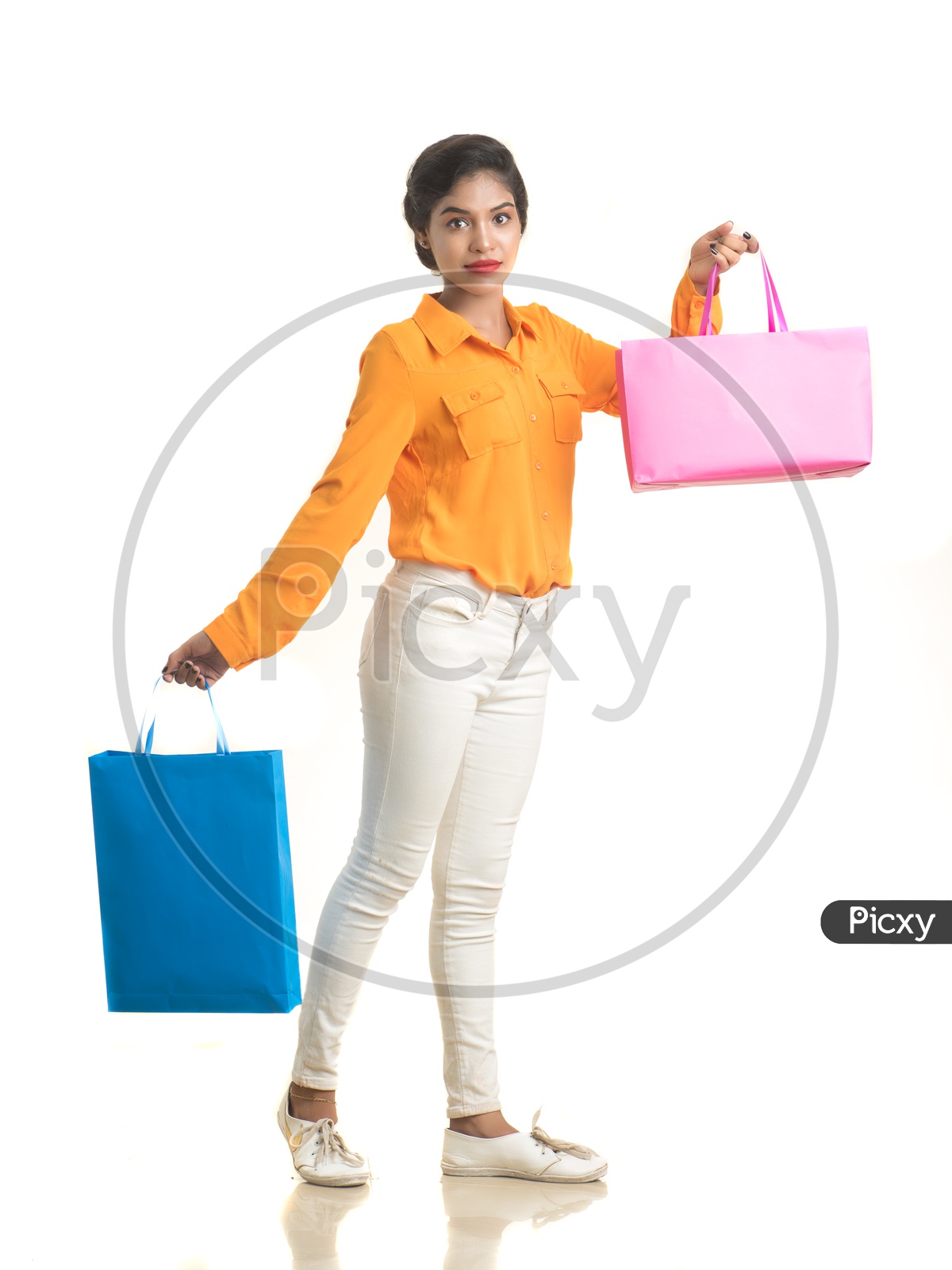Indian woman wearing orange shirt and white pant holding hand bags