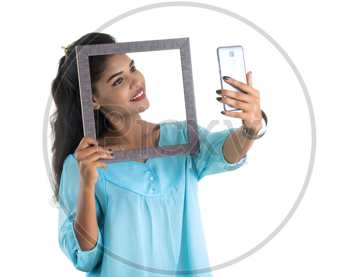 Pretty Young Indian Girl Posing With Photo Frames and a Mobile In Hand On an Isolated White Background
