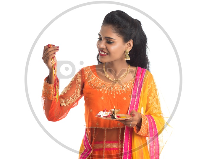 Young Indian Girl Holding Pooja Thali or Pooja Plate Along With an Elegant Rakhi For Her Brother  With a Smile Face on an Isolated White Background