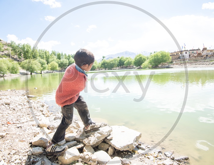 A Young Boy Throwing Stones To Slide Over The Water Surface Of a Lake In Village of Leh