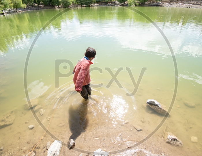 A Young Boy Throwing Stones To Slide Over The Water Surface Of a Lake In Village of Leh