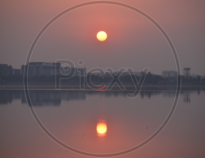 Reflection Of Buildings In Lake Water With Sun Set View