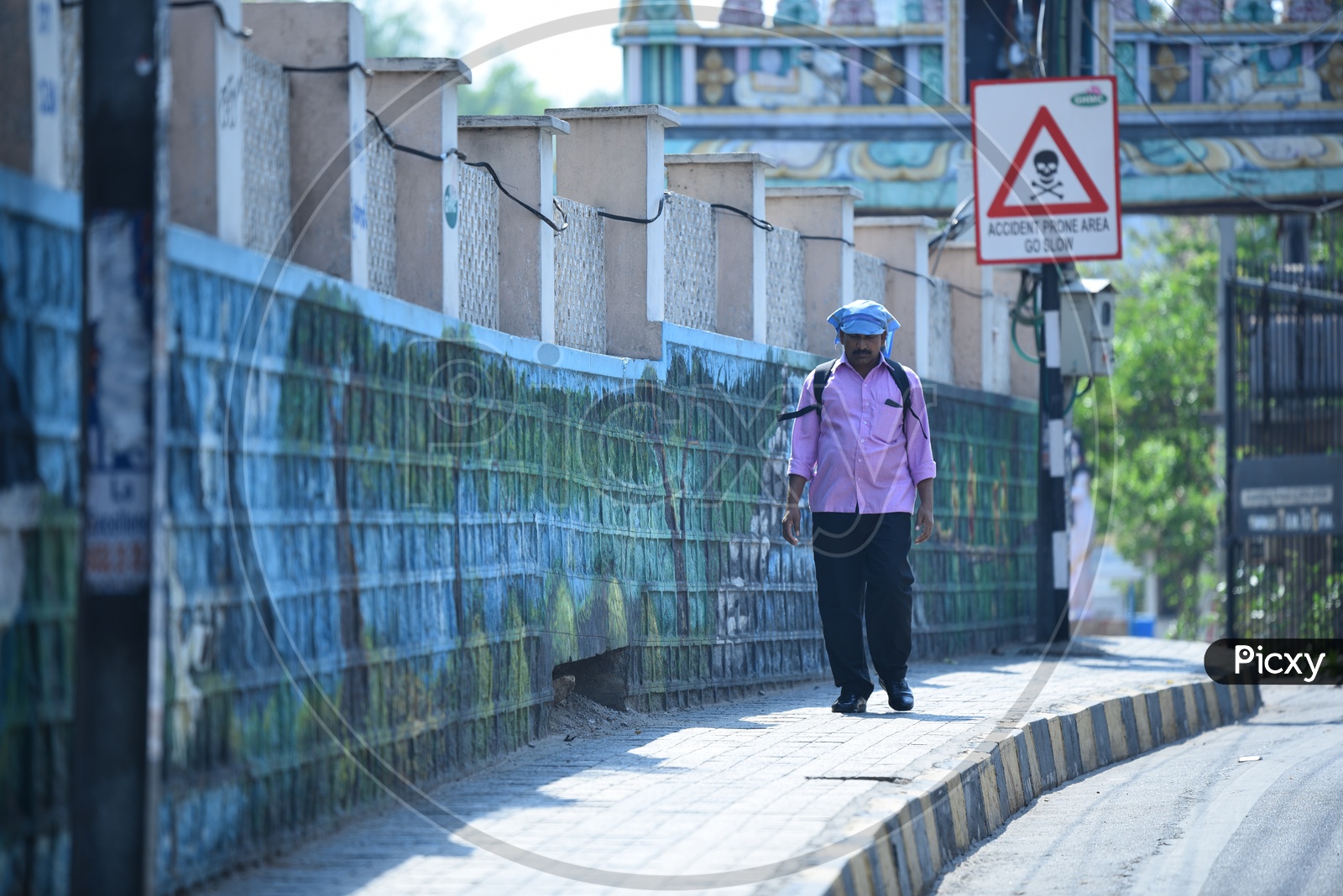 A Office Going Man Or Pedestrian Walking On  a Footpath in a Sunny day With Kerchief Covering His Head
