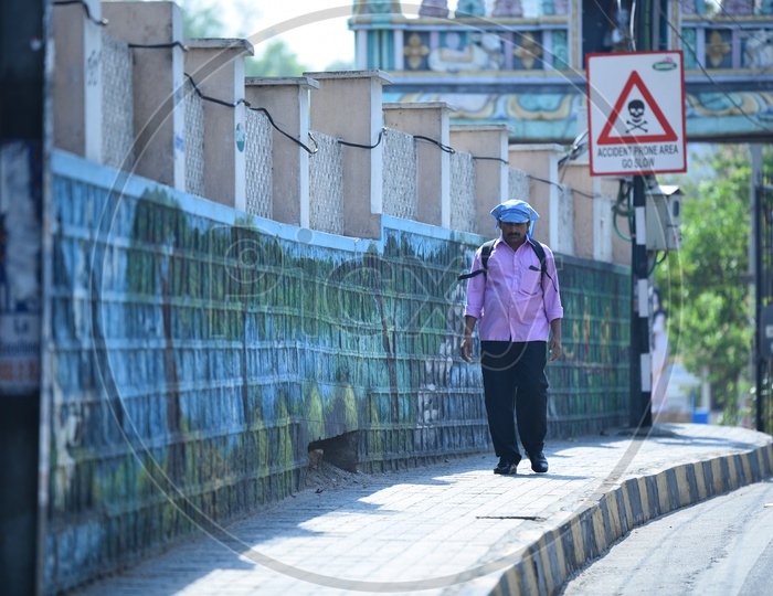A Office Going Man Or Pedestrian Walking On  a Footpath in a Sunny day With Kerchief Covering His Head