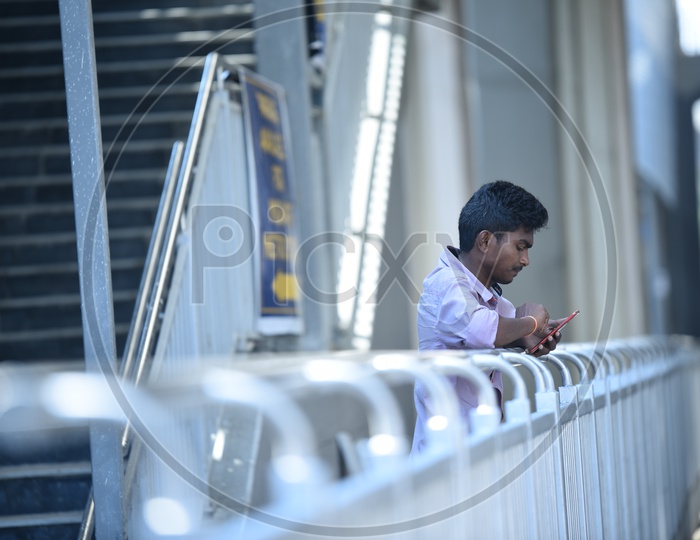 A Young Man Using Smart phone By Standing at A Metro Station Railing