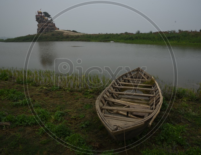A wooden boat near a pond and a temple on the stone hill in the background