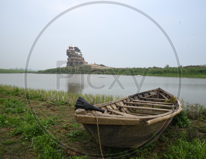 A wooden boat near a pond and a temple on the stone hill in the background