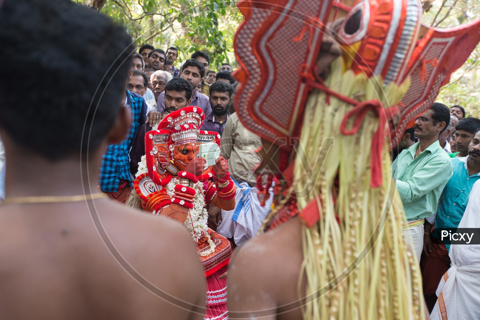 A Theyyam performer in colourful costume with a mirror