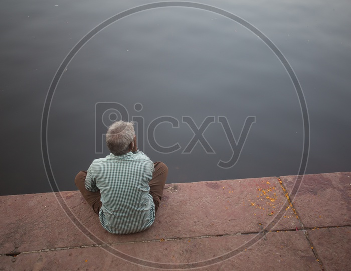 An elderly man sitting by the water side