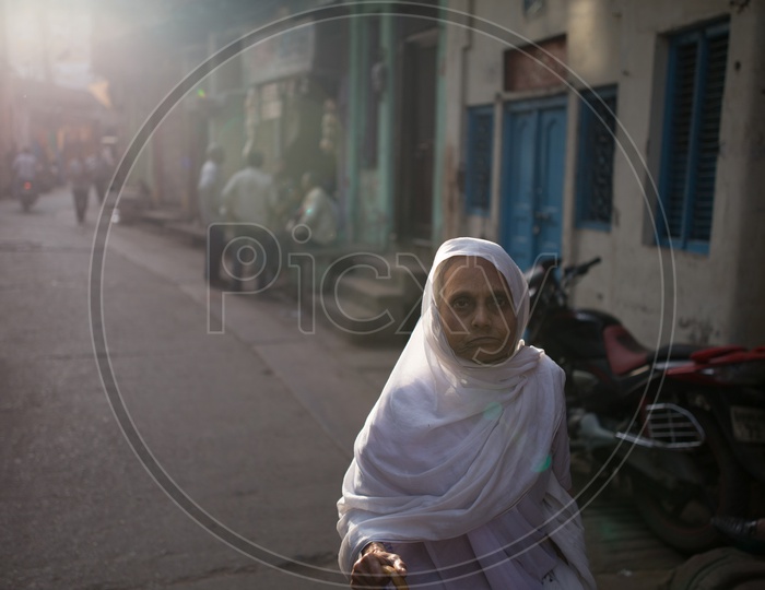 An Old Woman With White Veil Around Her Head Walking along The Streets In Barsana