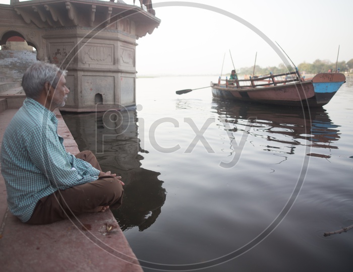 An elder man sitting by the riverside