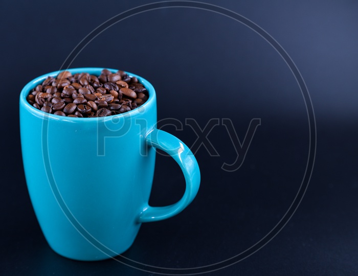 Coffee beans in a blue coffee mug on dark background