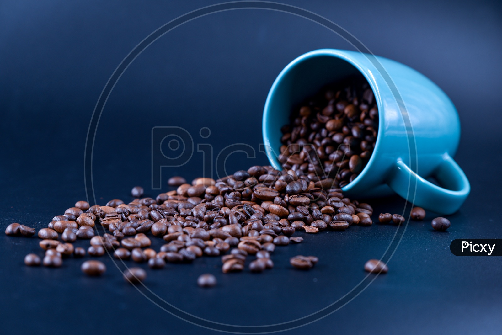 Coffee beans spilling out of a blue coffee mug on a dark background
