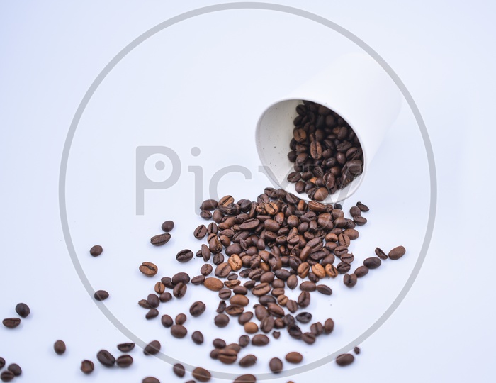 Coffee beans spilling out of a white take away cup on white background