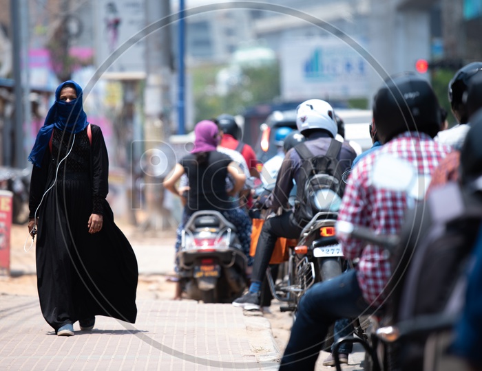 A Muslim Woman Wearing Burkha Walking On A Footpath with headphones on.