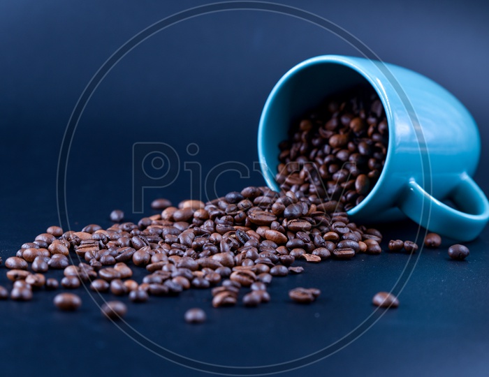 Coffee beans spilling out of a blue coffee mug on a dark background