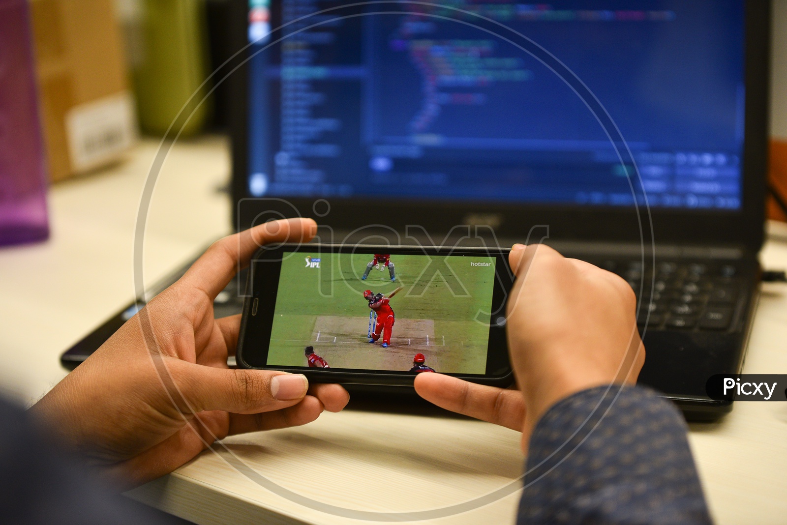 Image of Indian user watching IPL match on Hotstar app in Mobile while working in Office-JY050540-Picxy