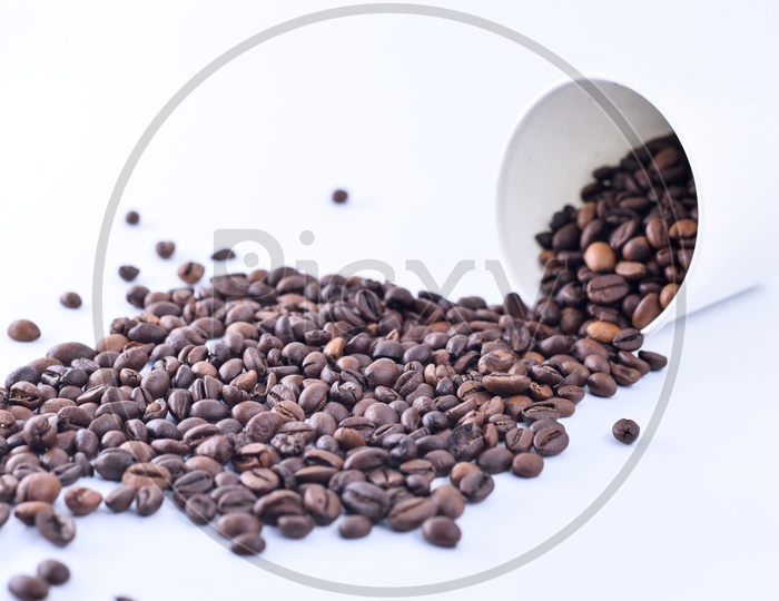 Coffee beans spilling out of a white take away cup on white background