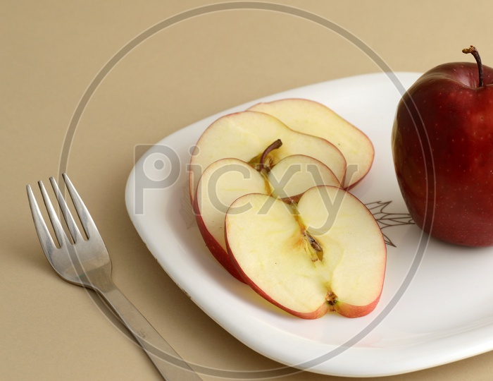 Fresh Red Apple Slices on White Plate With Fork and Knife On an Isolated Background