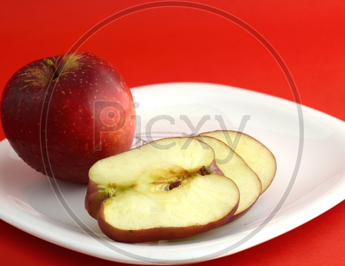 Ripen Red Apple Slices On White Plate Over an Isolated Red Background