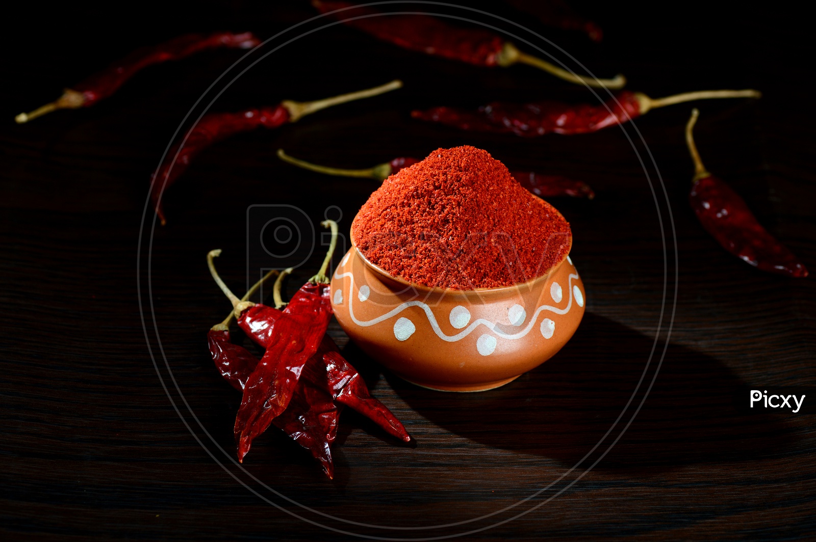 chilly powder in clay pot with red chilly, dried chillies on wooden background