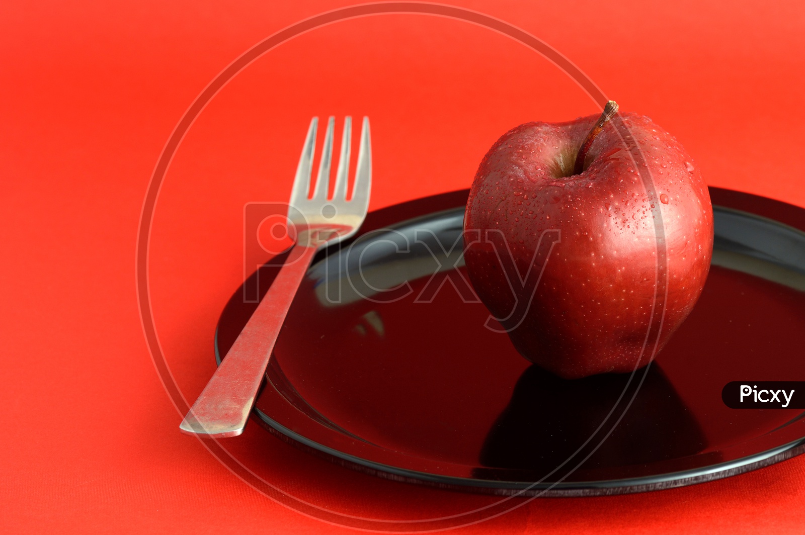 Ripen Red Apple on Black Plate With   Fork Over an Isolated Red Background