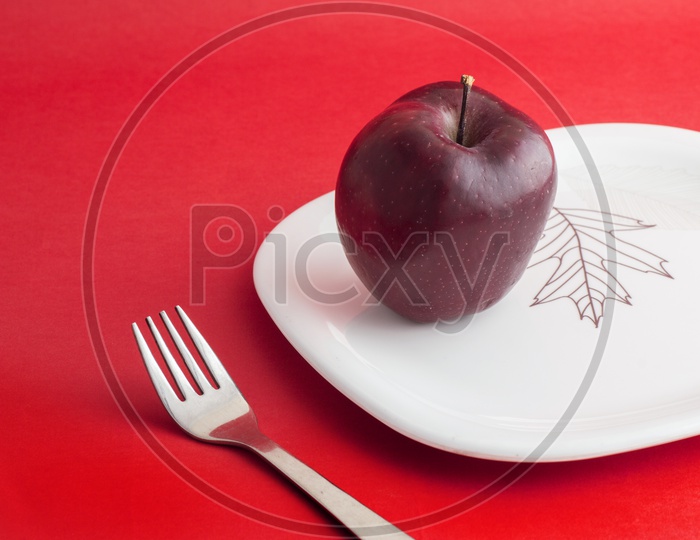 A Ripen Red Apple On White Plate With Fork  on an Isolated Red Background