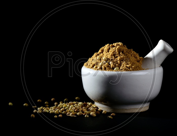 Coriander Powder and seeds with mortar and pestle on black background.