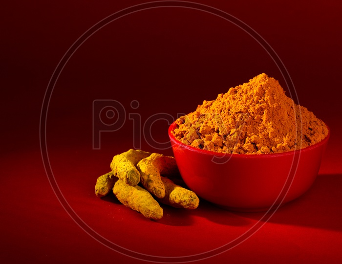 Dry Turmeric powder and roots or barks in red bowl on red background