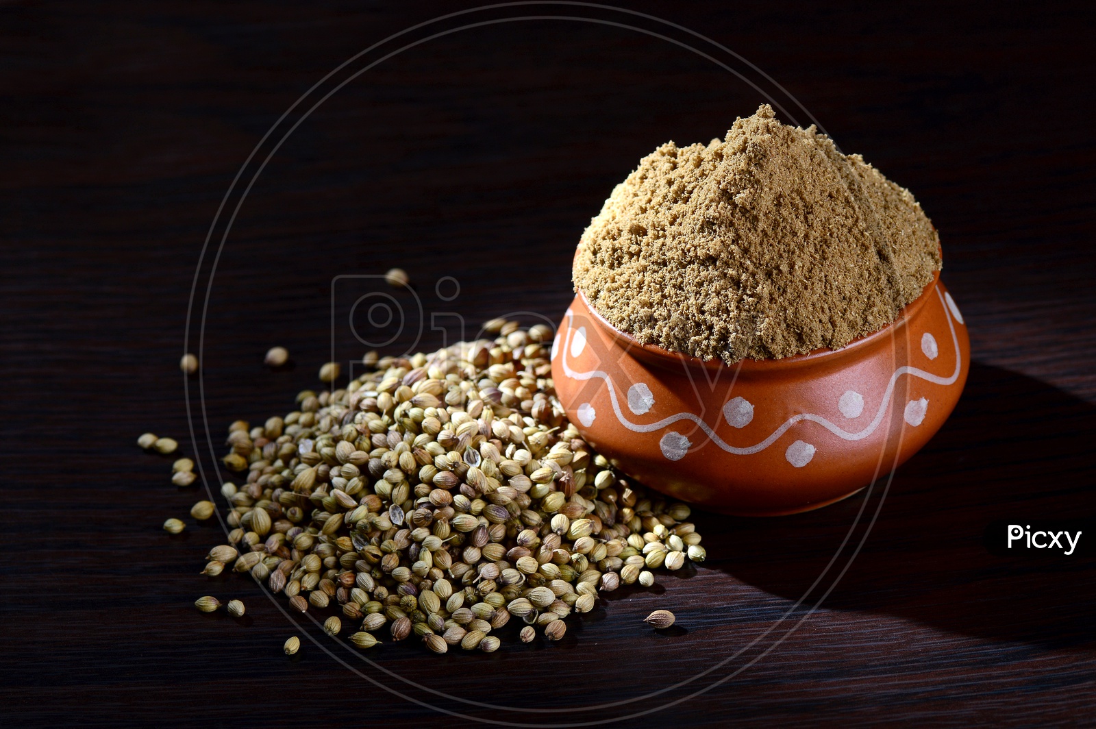 Coriander seeds and Powdered coriander in clay pot on wooden background.