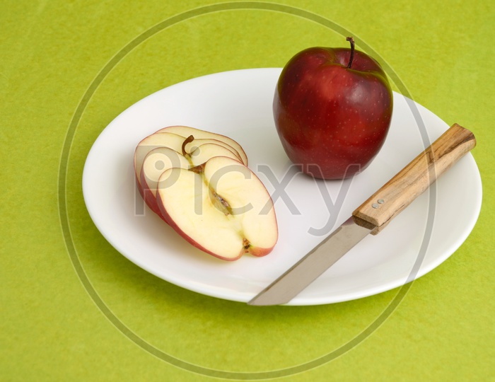 Fresh Red Apple Slices on White Plate With Fork and Knife On an Isolated Green  Background