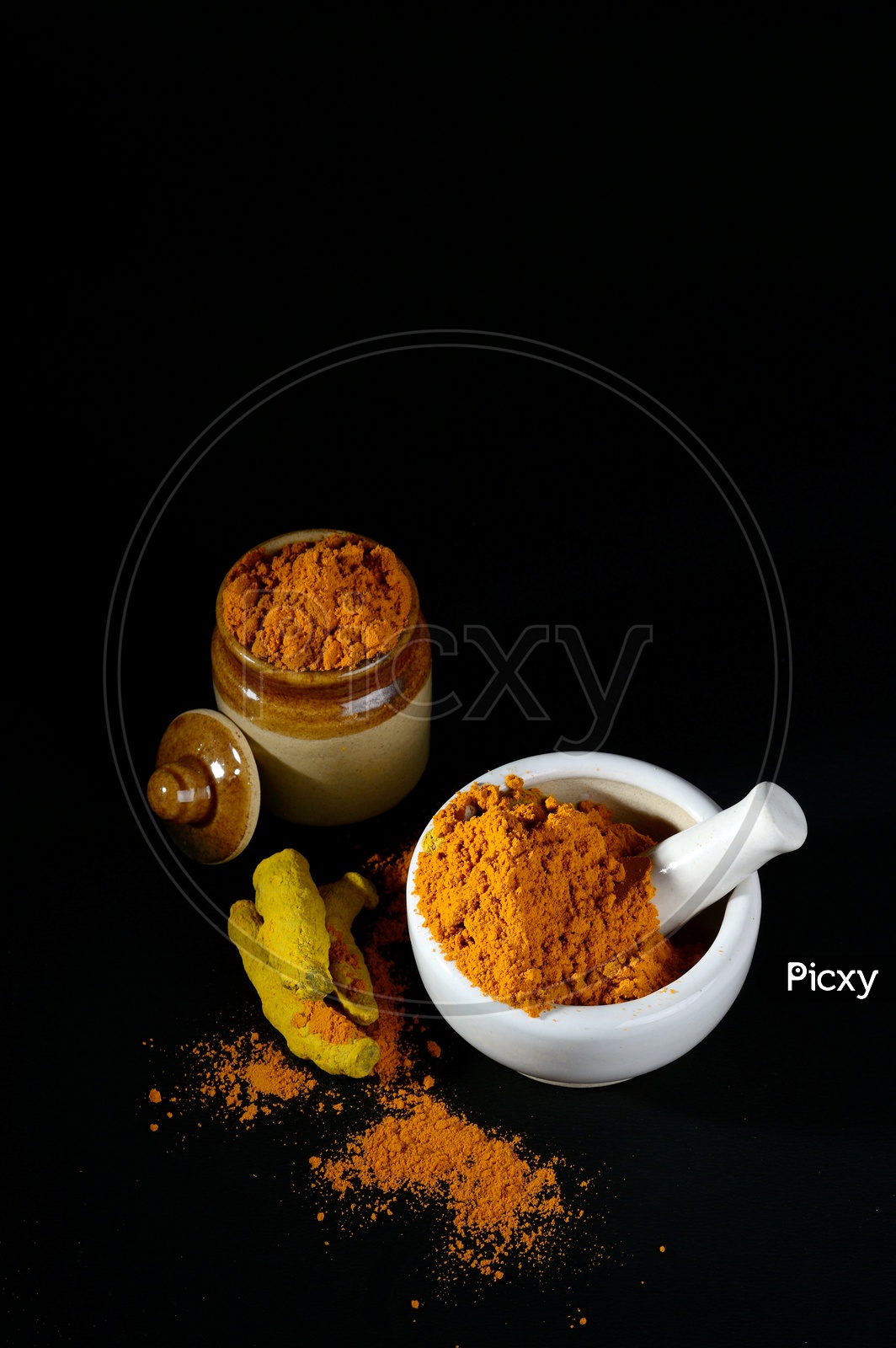 Turmeric powder in mortar with pestle and roots with clay pot on black background