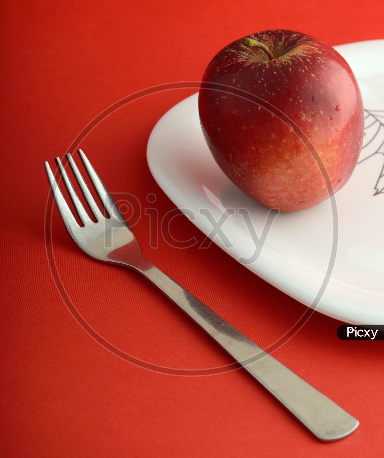 Ripen Red Apple On a White Plate With Fork On an Isolated  Red Background