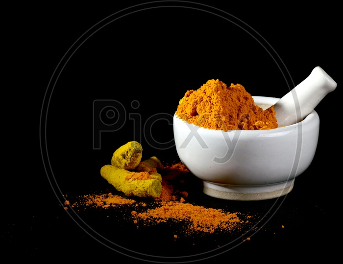 Turmeric powder in mortar with pestle and roots or barks on black background