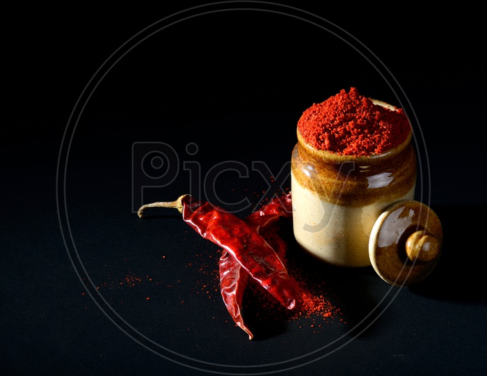 Red Chili Pepper powder in clay pot with Red Chili Peppers on black background