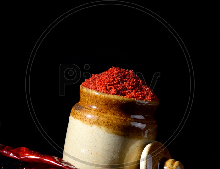 Red Chili Pepper powder in clay pot with Red Chili Peppers on black background