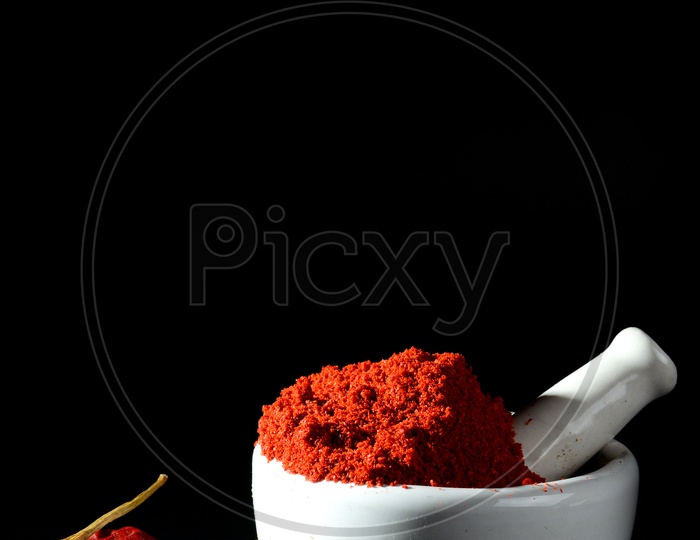 Red Chilli pepper powder in pestle with mortar and clay pot with Red Chilli Peppers on black background
