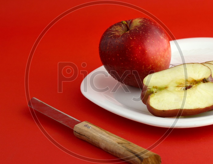 Ripen Red Apple Slices On White Plate With Knife  Over an Isolated Red Background