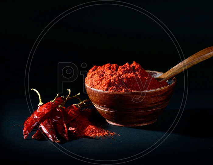 chilly powder in wooden bowl with red chilly, dried chillies on black background