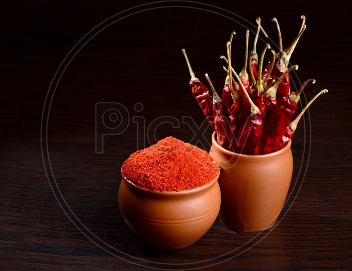 chilly powder with red chilly in clay pots, dried chillies on dark background
