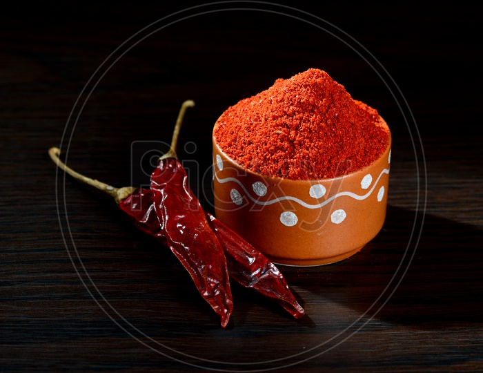 chilly powder in clay pot with red chilly, dried chillies on wooden background